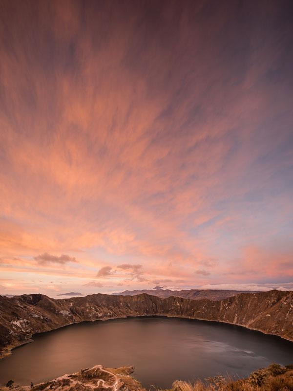 A vertical image of Laguna de Quilotoa during sunset in the Andes.