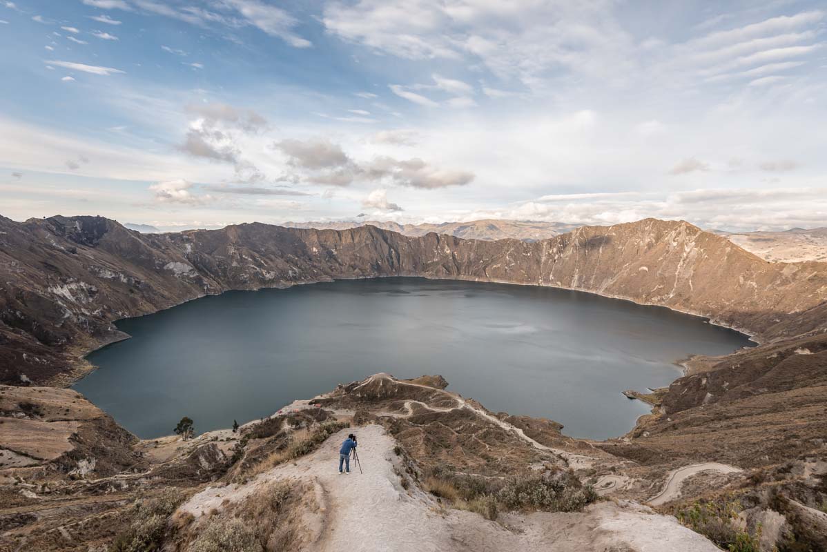 A crater lake surrounded by the Andes mountains is photographed by a lone photographer