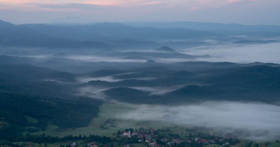 Early morning sunlight creeps across a rural farmers meadow in Slovenia, photographed from a high perch on Nanos Mountain on the Via Dinarica White Trail.