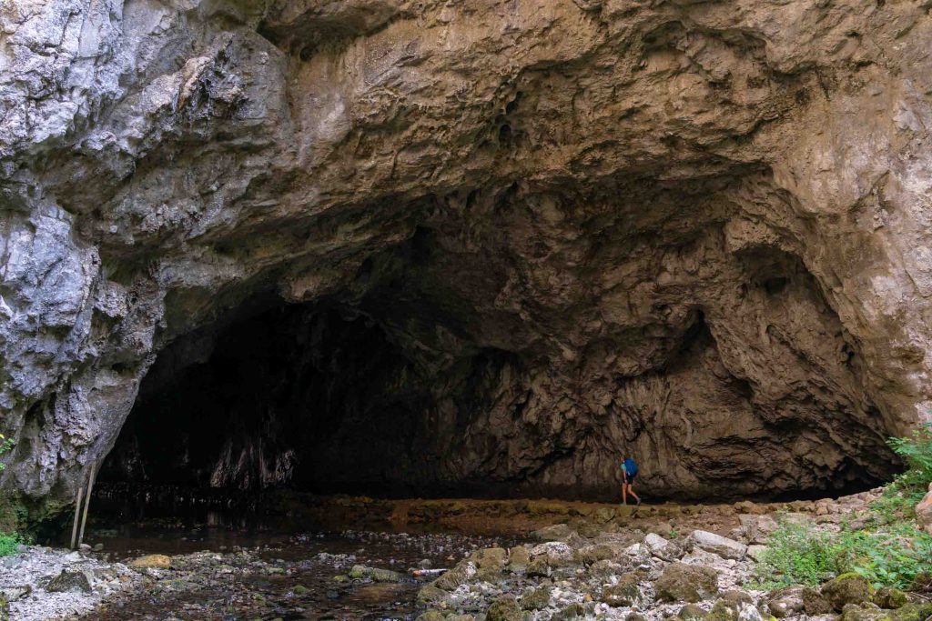 A hiker walks into massive limestone caves found along the Via Dinarica White Trail in Slovenia.